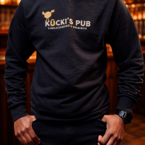 Black Kücki’s Pub sweatshirt with logo, standing inside a warm, traditional pub setting.