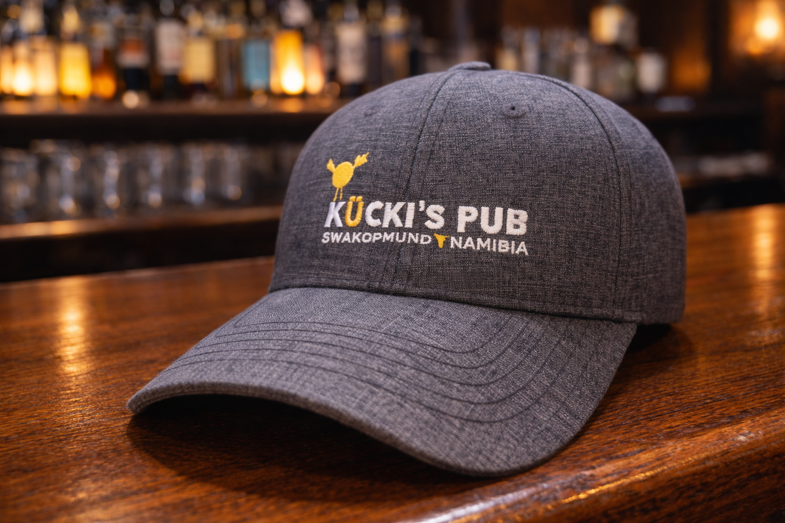 Kucki's Pub charcoal grey baseball cap with embroidered white logo and gold ostrich graphic, Swakopmund Namibia merchandise