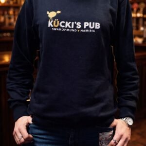 Woman wearing a black Kücki’s Pub sweatshirt with logo, standing in a warm, traditional pub setting.
