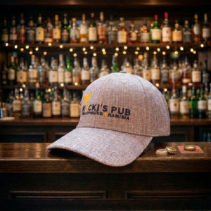 Light grey triblend snapback cap featuring the embroidered Kücki's Pub Swakopmund Namibia logo on a dark wooden bar counter with beer caps, in a brightly lit bar setting.