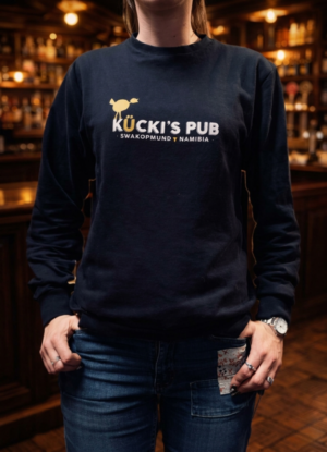 Woman wearing a black Kücki’s Pub sweatshirt with logo, standing in a warm, traditional pub setting.